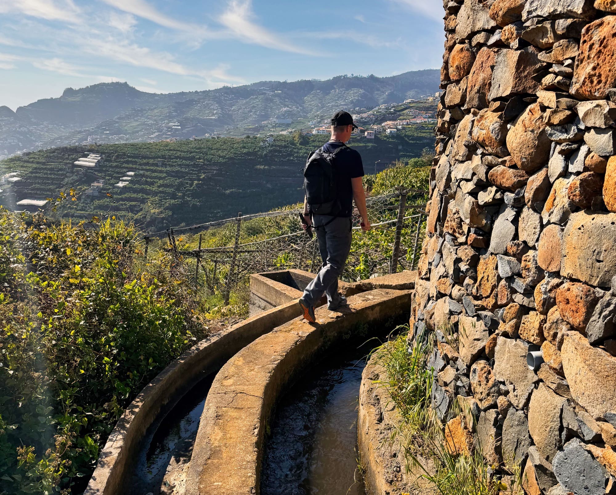 Hiker on Levada dos Piornais path beside terraced banana plantations and stonewall.